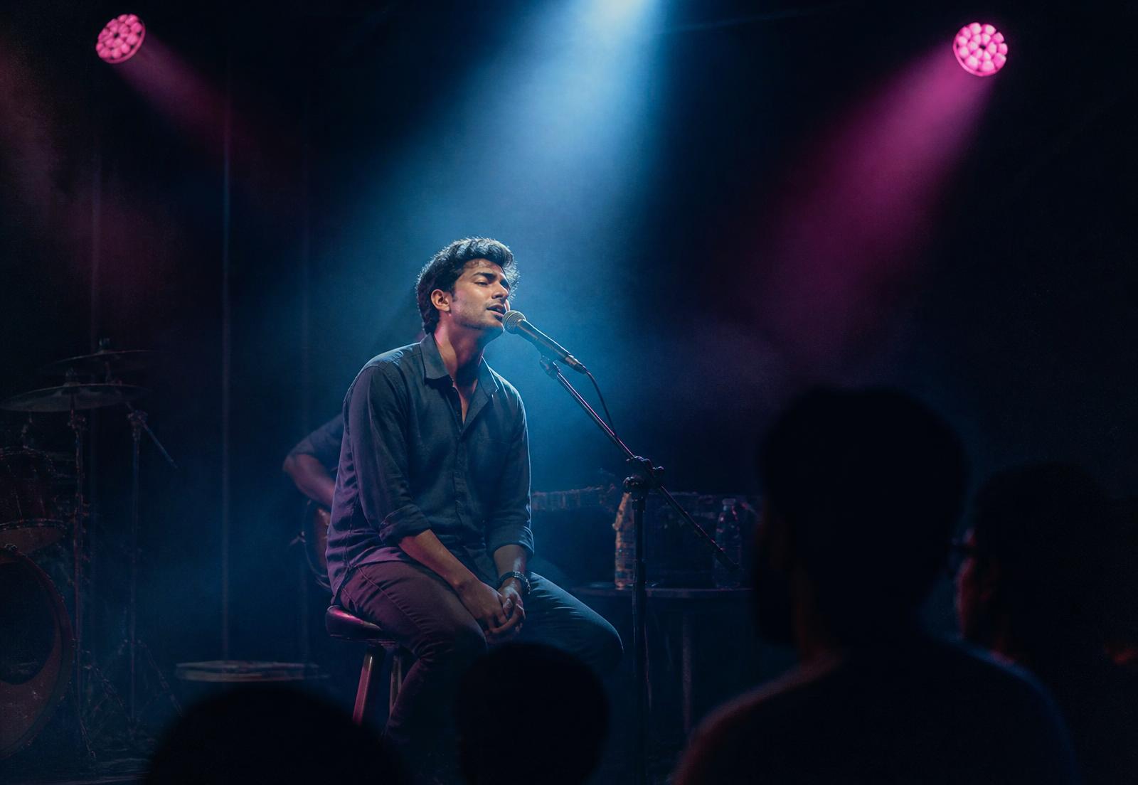 Singer performing on a small stage under a spotlight with pink stage lights